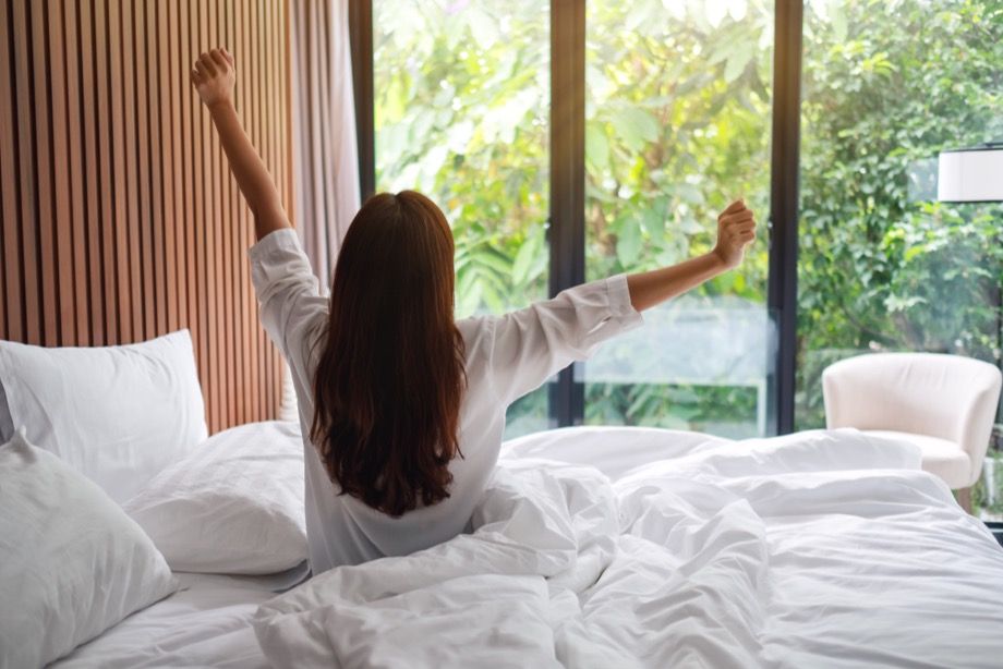 Morning look. Фон утро окно зарядка. Rear view of a woman do stretching after waking up in the morning.